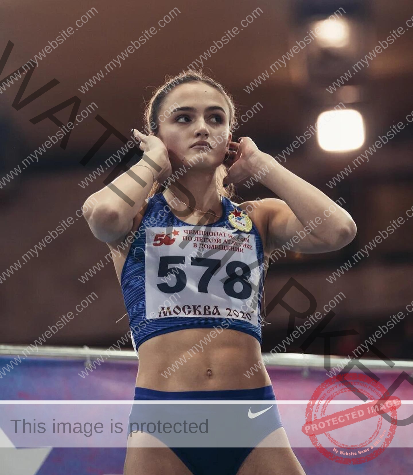 polina-tkalich-russia-p_a_tkalich-11522 Polina Tkalich, track and field star from Russia, adjusts her hair in a blue outfit, bib 578, looking focused before competing indoors.