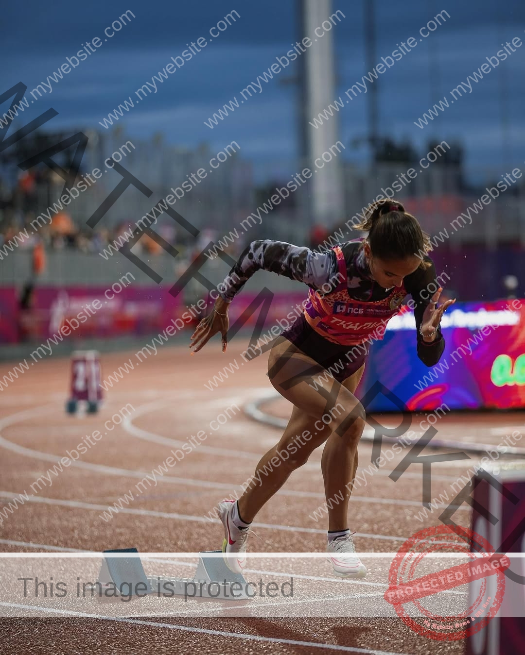 polina-tkalich-russia-p_a_tkalich-12108 Polina Tkalich, track and field star from Russia, launches off the starting blocks on a track, stadium and crowd under a cloudy sky.