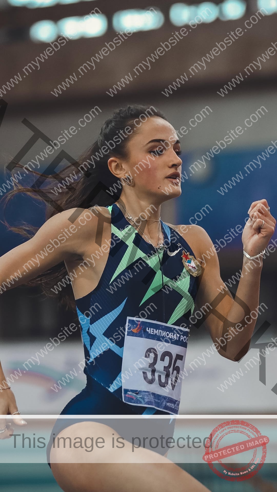polina-tkalich-russia-p_a_tkalich-12183 Polina Tkalich, track and field star from Russia, in a blue and green star uniform runs indoors with race bib 335, focused.