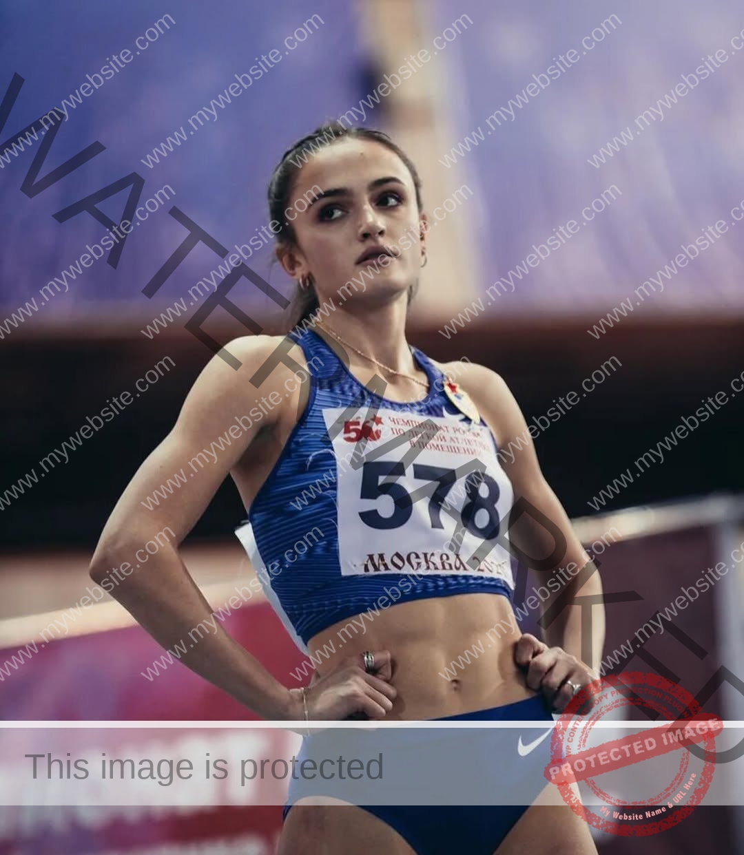 polina-tkalich-russia-p_a_tkalich-12497 Polina Tkalich, track and field star from Russia, stands with hands on hips in a blue outfit and bib 578, looking focused indoors.