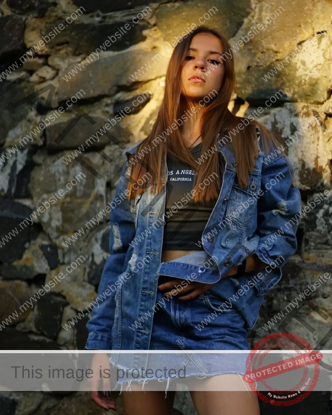 rufina-kotik-ukraine-rufina.kotik14-u18-01712 Rufina Kotik, track and field star from Ukraine, in a distressed denim jacket and skirt by a stone wall, sunlight on her face.