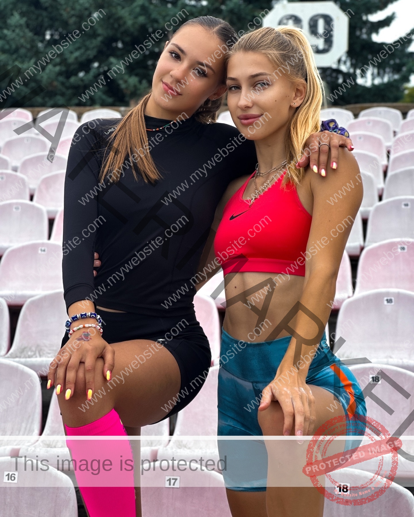 rufina-kotik-ukraine-rufina.kotik14-u18-01862 Rufina Kotik, track and field star from Ukraine, poses in athletic wear with a friend in an empty stadium, both smiling and posing.