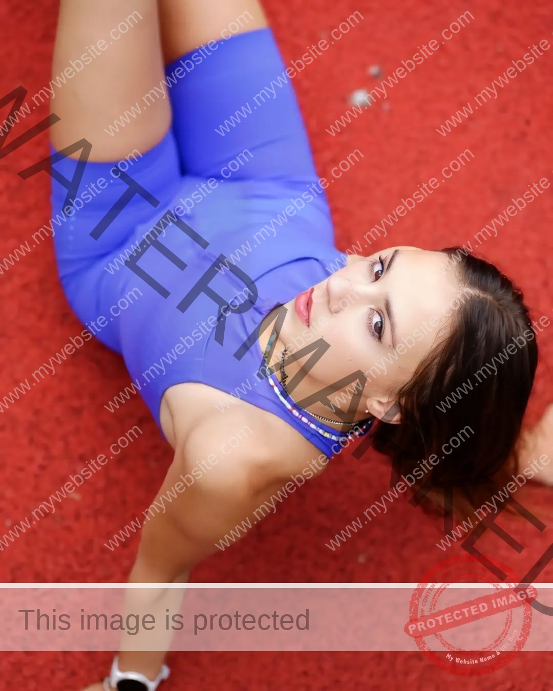 rufina-kotik-ukraine-rufina.kotik14-u18-01876 Rufina Kotik, track and field star from Ukraine, in blue athletic wear sits on red surface, looking up seriously; beaded necklaces, white sneakers.