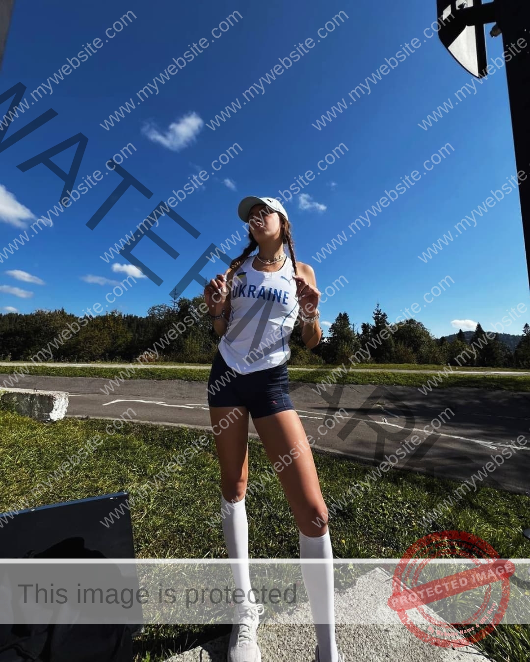 rufina-kotik-ukraine-rufina.kotik14-u18-01904 Rufina Kotik, track and field star from Ukraine, poses confidently outdoors in a white UKRAINE tank top, navy shorts, knee-high socks.