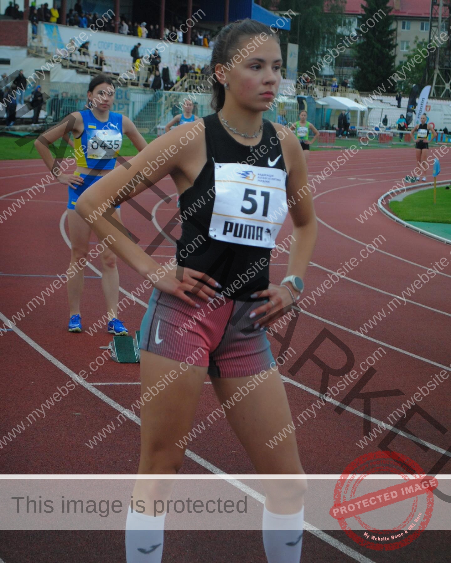 rufina-kotik-ukraine-rufina.kotik14-u18-02011 Rufina Kotik, track and field star from Ukraine, stands on the running track in black top, red shorts (51), hands on hips.