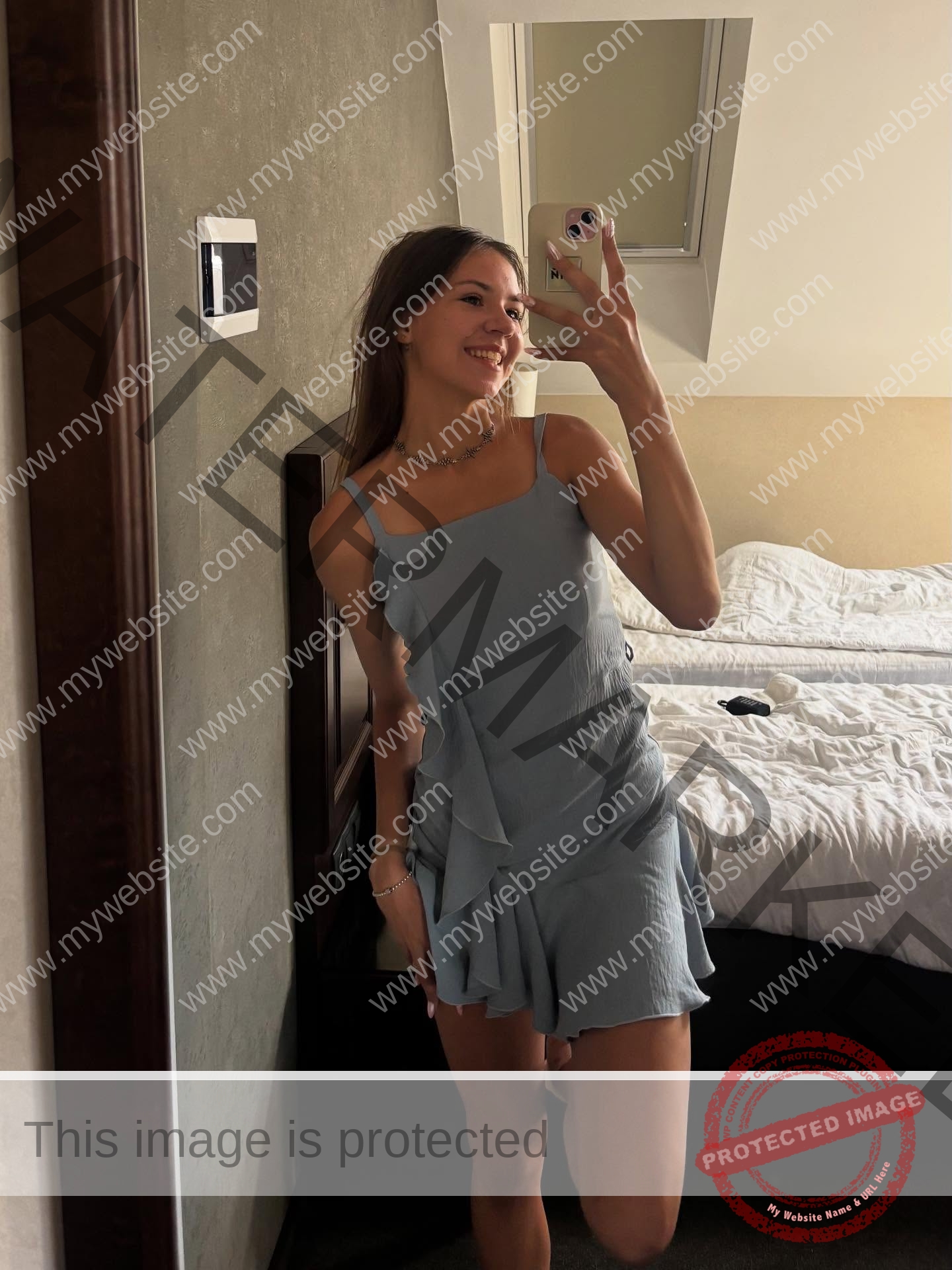 rufina-kotik-ukraine-rufina.kotik14-u18-02037 Rufina Kotik, track and field star from Ukraine, wearing a light blue dress, smiles taking a selfie by a mirror; bed behind her.