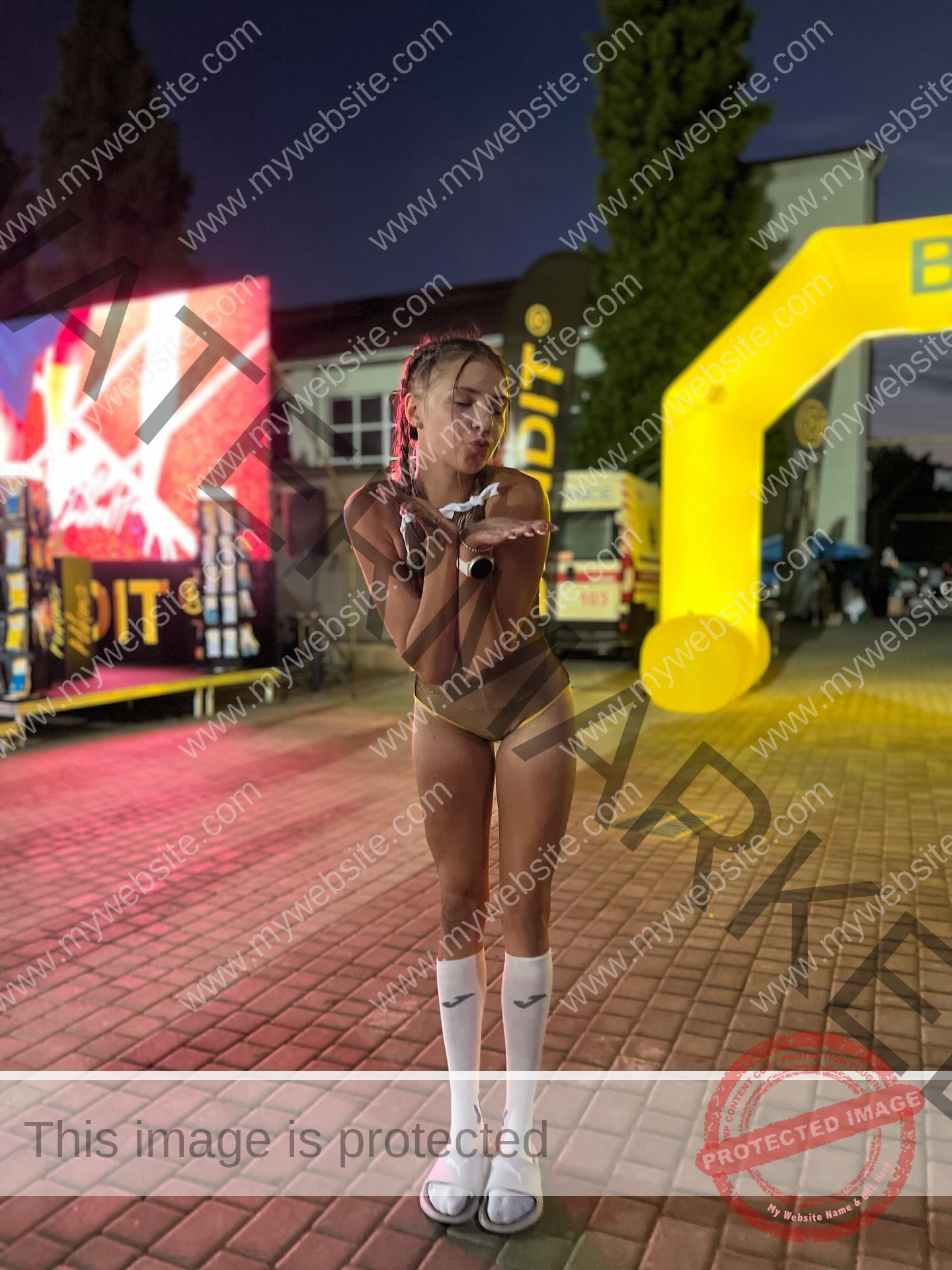 rufina-kotik-ukraine-rufina.kotik14-u18-02046 Rufina Kotik, track and field star from Ukraine, in yellow bikini and white socks blows a kiss on brick pavement at night.
