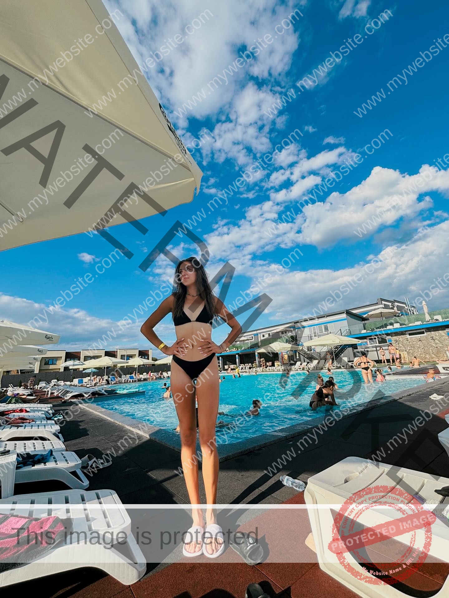 rufina-kotik-ukraine-rufina.kotik14-u18-02058 Rufina Kotik, track and field star from Ukraine, stands poolside in a black and white bikini as others relax under a sunny sky.