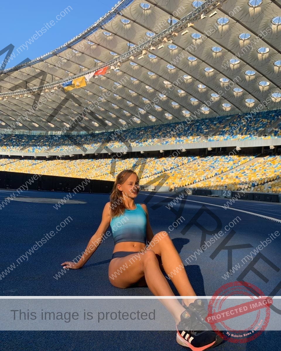 sasha-liubanska-ukraine-sasha_liubanska-u20-x-06009 Sasha Liubanska, track and field star from Ukraine, sits on a stadium track in athletic wear as sunlight casts dramatic shadows.