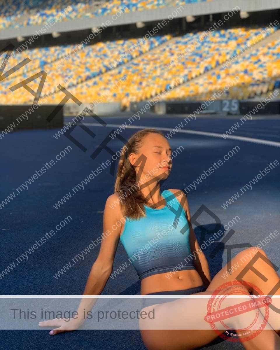 sasha-liubanska-ukraine-sasha_liubanska-u20-x-06010 Sasha Liubanska, track and field star from Ukraine, in athletic wear on a blue track, relaxing with eyes closed under the sun.