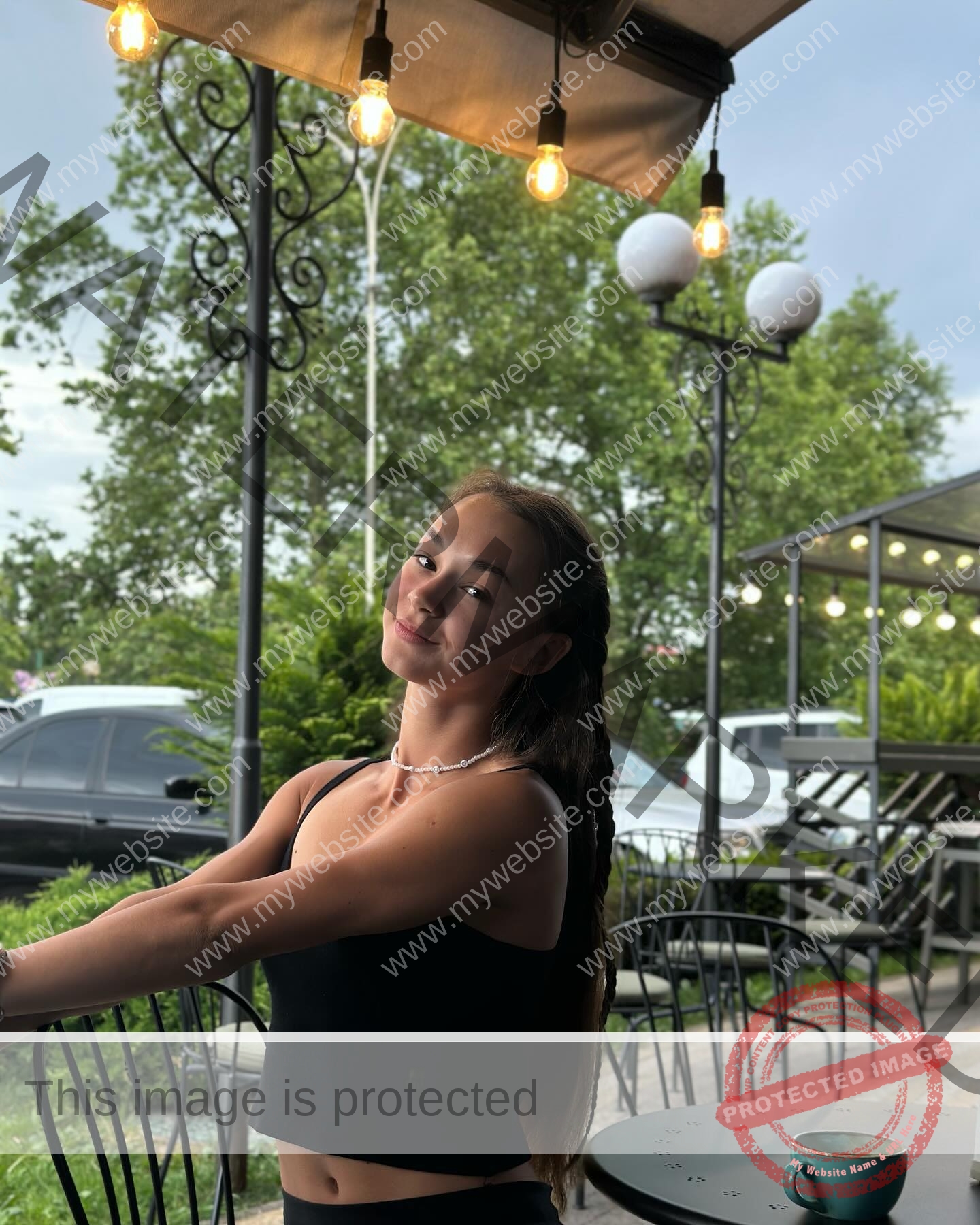 sasha-liubanska-ukraine-sasha_liubanska-u20-x-06033 Sasha Liubanska, track and field star from Ukraine, with long brown hair, smiles at an outdoor café table under hanging lights.