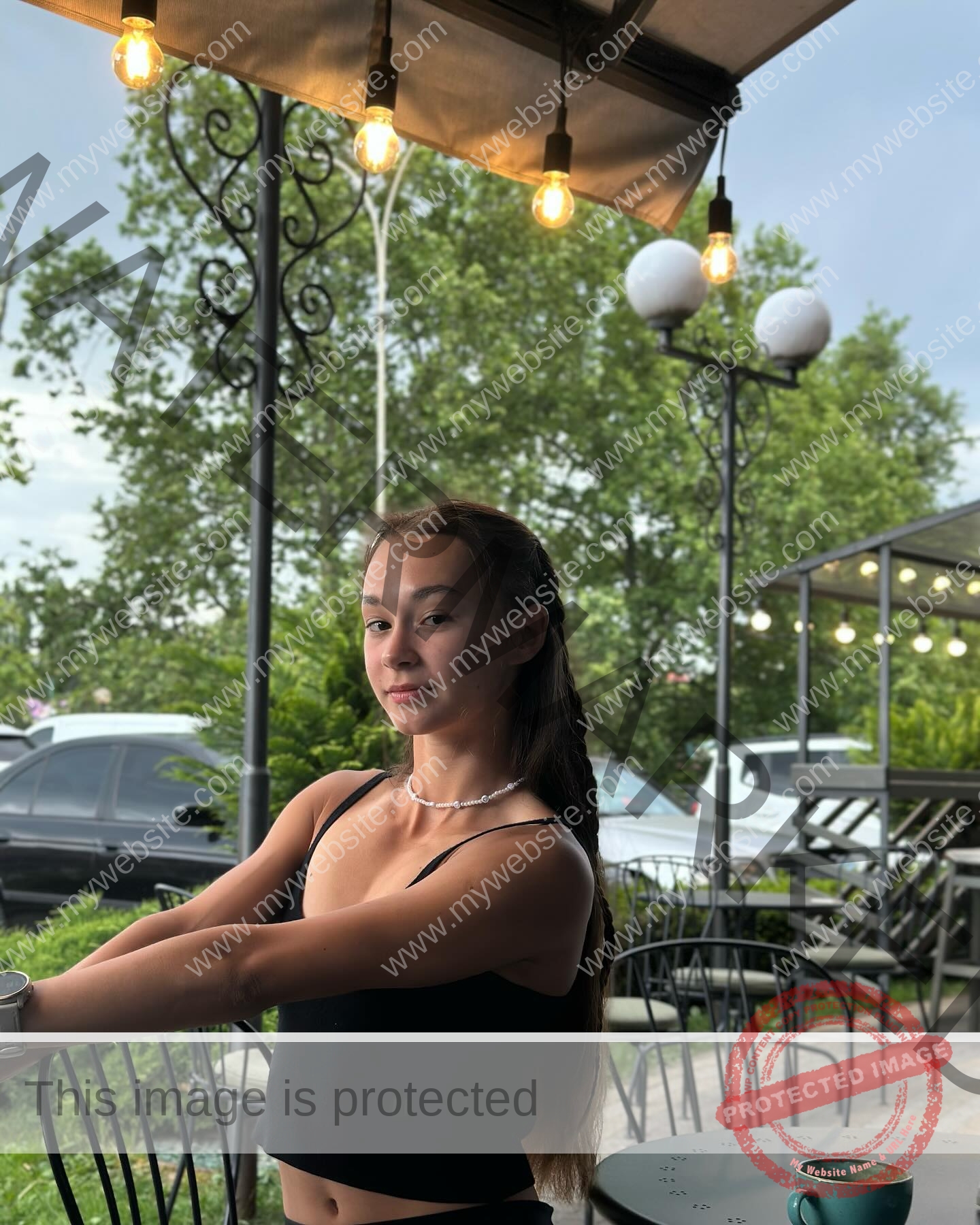 sasha-liubanska-ukraine-sasha_liubanska-u20-x-06034 Sasha Liubanska, track and field star from Ukraine, with long brown hair in a black crop top poses at an outdoor café at night.