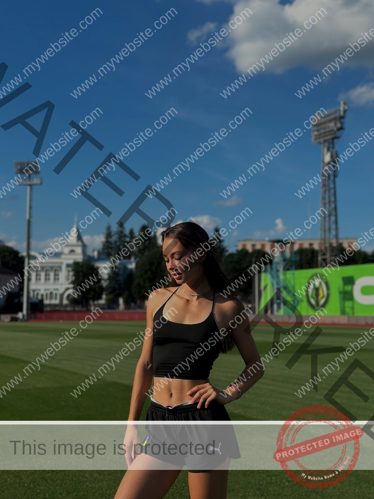 sasha-liubanska-ukraine-sasha_liubanska-u20-x-06066 Sasha Liubanska, track and field star from Ukraine, stands in a black sports outfit on a green field under a clear blue sky.