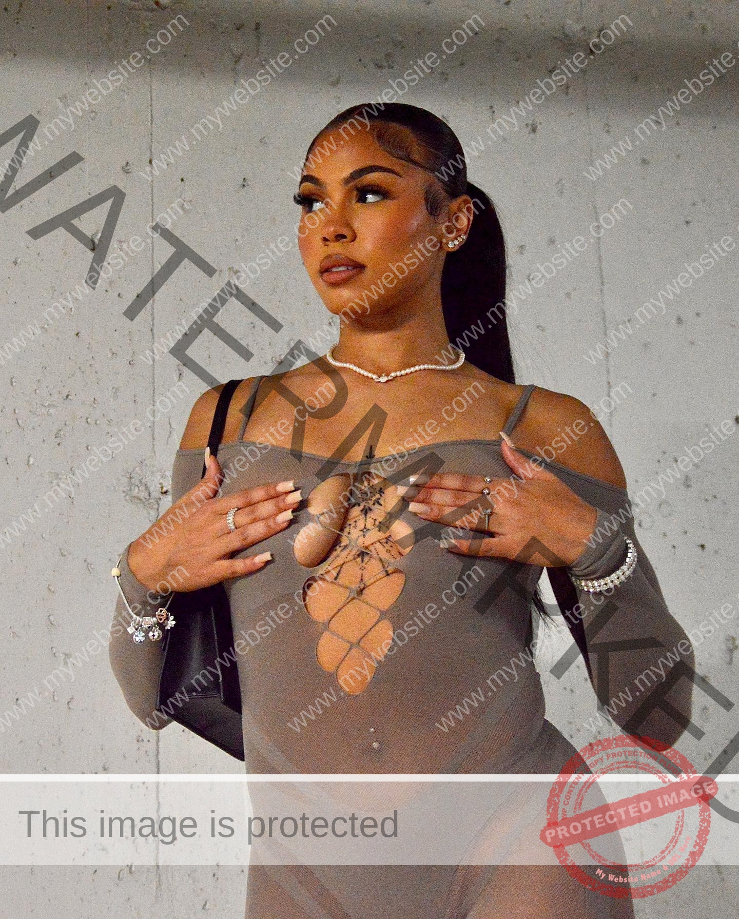 tatiana-aholou-canada-tatianaaholou-00425 Tatiana Ahoulou, track and field star from Canada, stands by a concrete wall in a sheer gray dress with chest cut-outs, gazing aside.