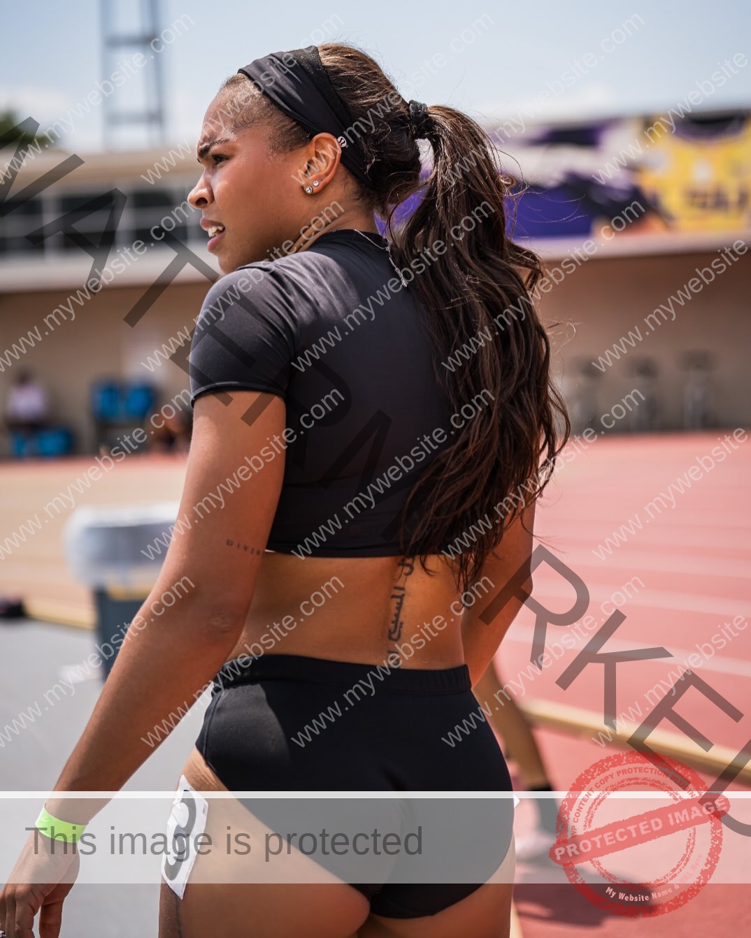tatiana-aholou-canada-tatianaaholou-00500 Tatiana Ahoulou, track and field star from Canada stands on a track in black gear, ponytail up, race number 3 and tattoo visible.