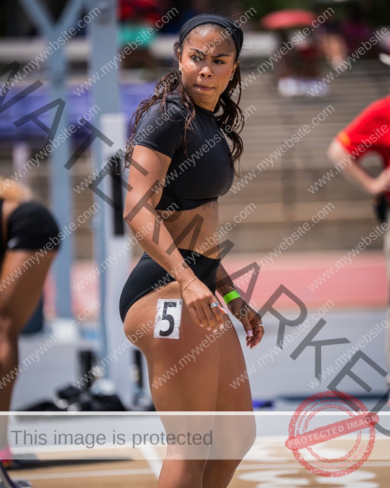tatiana-aholou-canada-tatianaaholou-00501 Tatiana Ahoulou, track and field star from Canada, in a black outfit with number 5 tag stands on a track, looking to the side.
