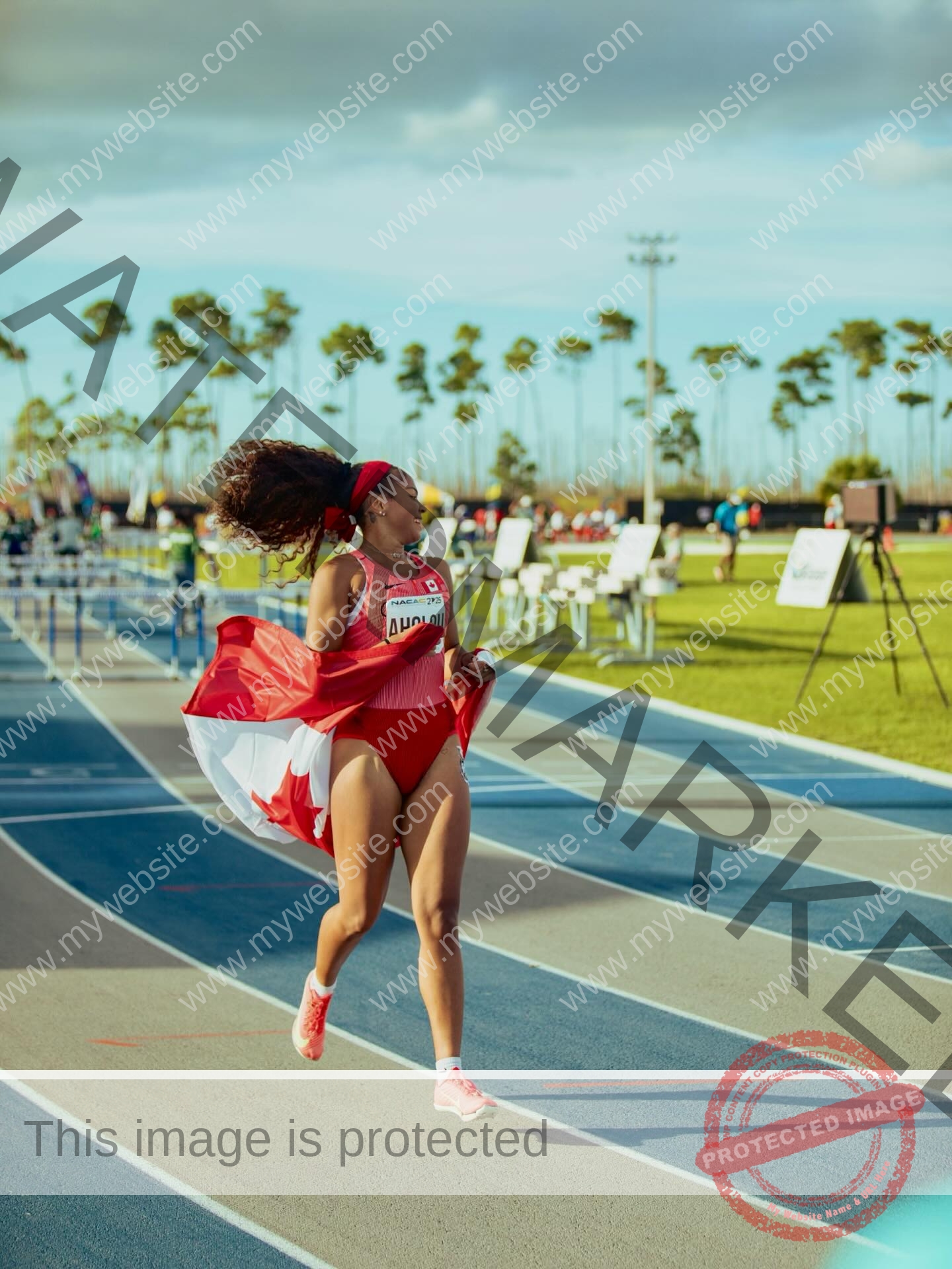 tatiana-aholou-canada-tatianaaholou-00503 Tatiana Ahoulou, track and field star from Canada, wearing red and holding a flag, runs joyfully on a blue track with palm trees.