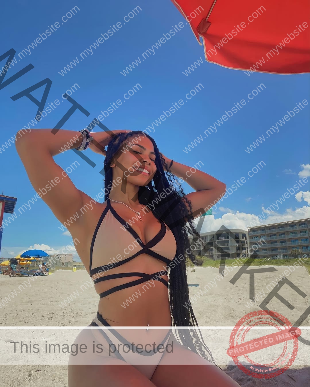 tatiana-aholou-canada-tatianaaholou-00521 Tatiana Ahoulou, track and field star from Canada, smiles in a beige bikini with long braids on a sunny beach under a red umbrella.