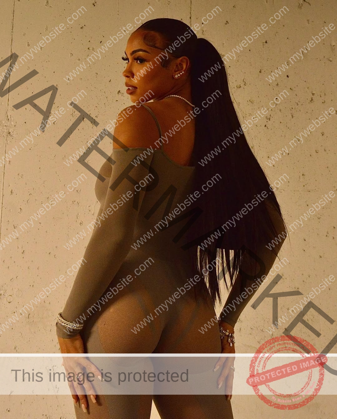 tatiana-aholou-canada-tatianaaholou-00541 Tatiana Ahoulou, track and field star from Canada, poses with back turned in a sheer taupe bodysuit, glancing over her shoulder.