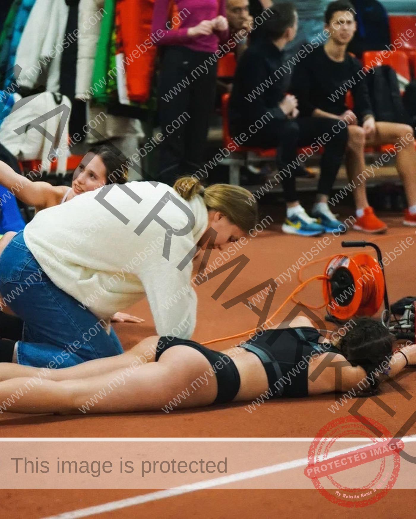 viktoriya-antipova-russia-viichkaaaaa-03536 Viktoriya Antipova, track and field star from Russia, lies face down on an indoor track as another woman kneels to assist her.