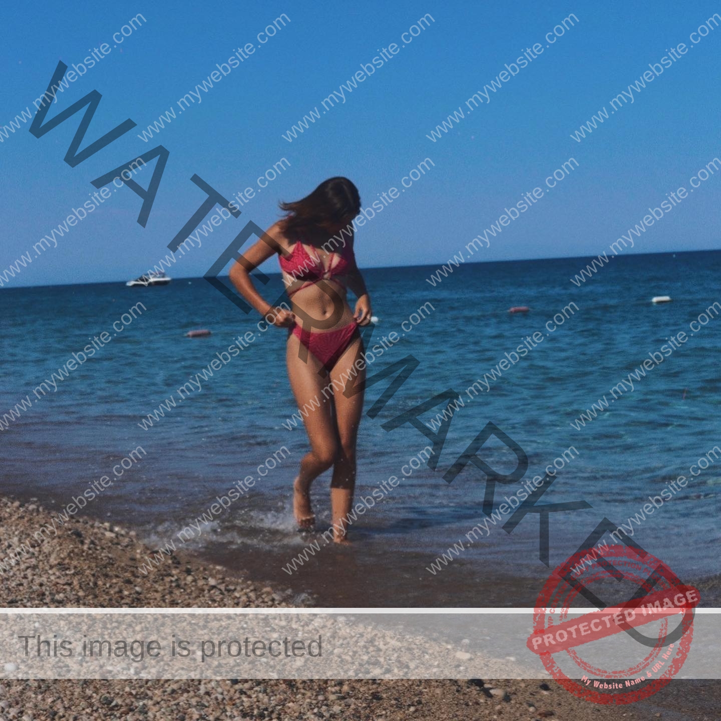 viktoriya-antipova-russia-viichkaaaaa-03544 Viktoriya Antipova, track and field star from Russia, stands in a red bikini on a pebbly beach with calm sea and distant boat.