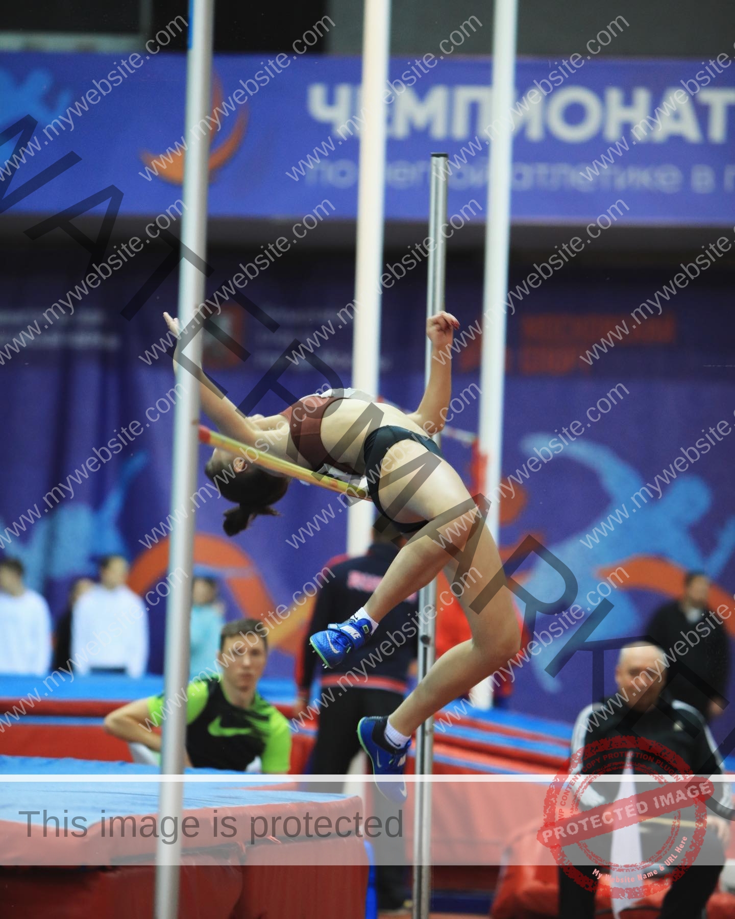 viktoriya-antipova-russia-viichkaaaaa-03558 Viktoriya Antapova, track and field star from Russia, soars mid-air in a high jump as officials and spectators watch closely.