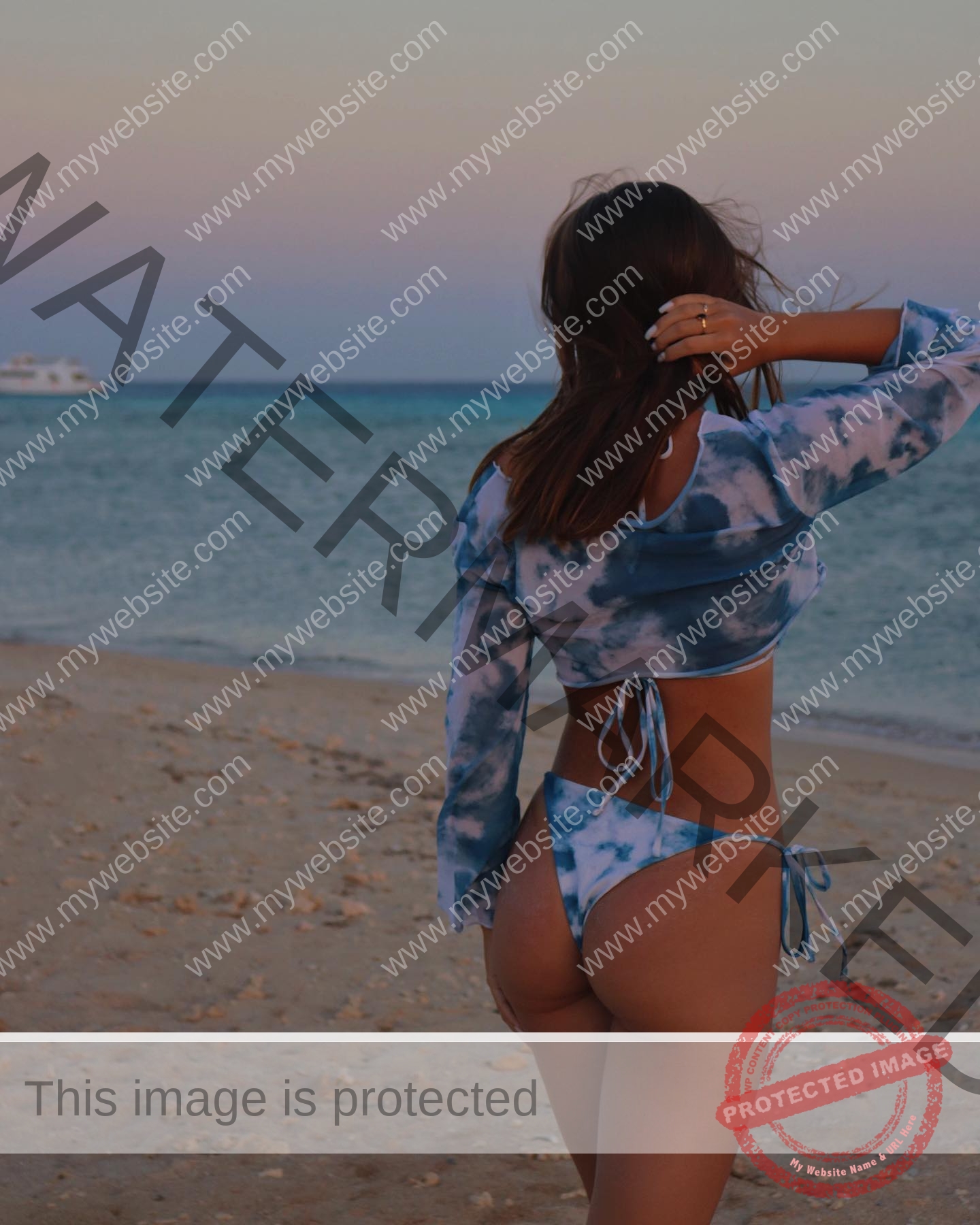 viktoriya-antipova-russia-viichkaaaaa-03584 Viktoriya Antapova, track and field star from Russia, in a blue tie-dye bikini on the beach at sunset, hand in hair, boat distant.