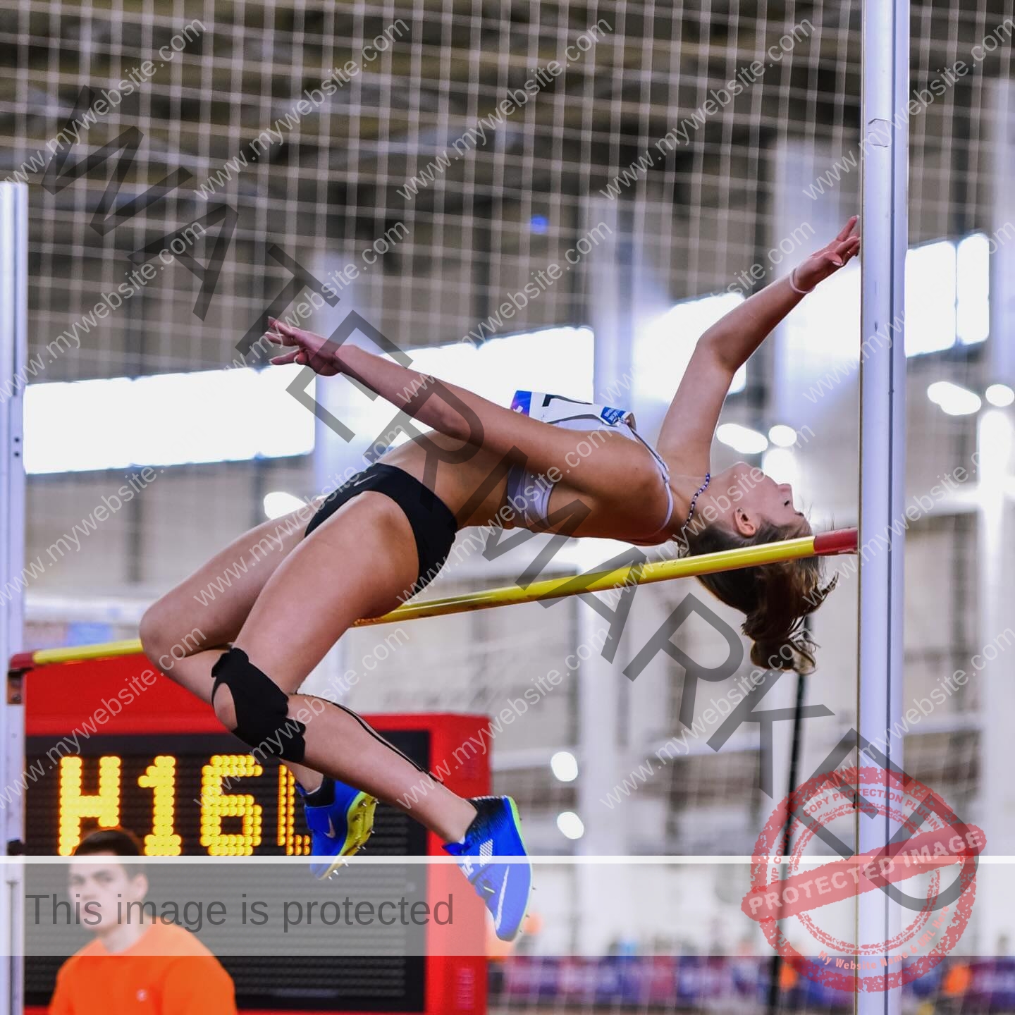 viktoriya-antipova-russia-viichkaaaaa-03615 Viktoriya Antipova, track and field star from Russia, performs a high jump indoors, arching over the bar with a digital scoreboard behind.