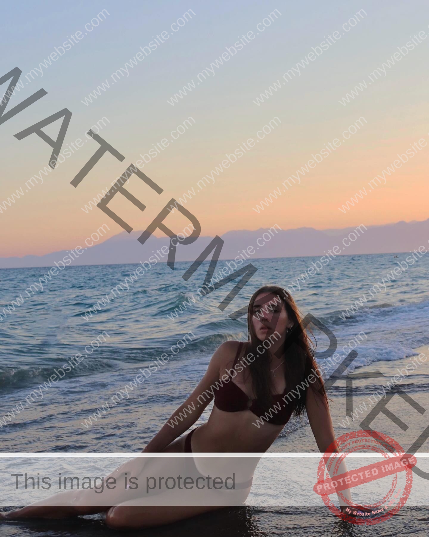 viktoriya-antipova-russia-viichkaaaaa-03661 Viktoriya Antipova, track and field star from Russia, in a burgundy bikini sits on wet sand by the sea at sunset with soft waves.