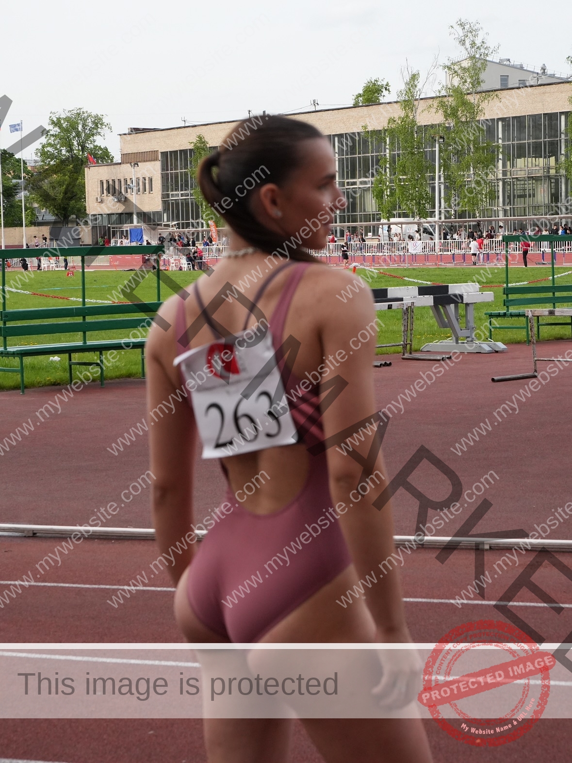 viktoriya-antipova-russia-viichkaaaaa-03733 Viktoriya Antipova, track and field star from Russia, stands on a track in pink with 263 on her back, facing away.