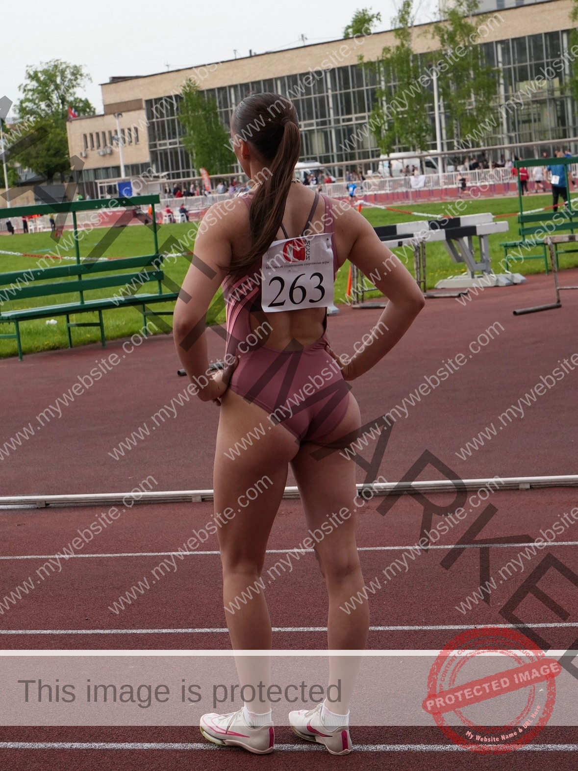 viktoriya-antipova-russia-viichkaaaaa-03735 Viktoriya Antipova, track and field star from Russia, stands on a track in mauve leotard, hands on hips, bib 263 visible.