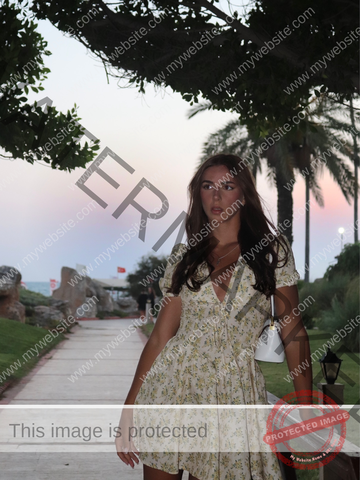 viktoriya-antipova-russia-viichkaaaaa-03744 Viktoriya Antapova, track and field star from Russia, in a yellow floral dress holding a purse, stands by palms at sunset.