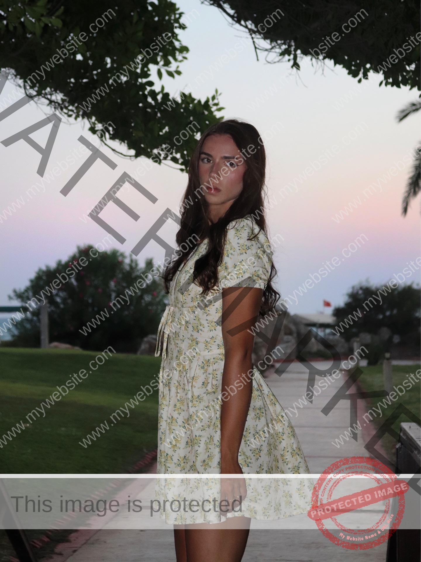 viktoriya-antipova-russia-viichkaaaaa-03746 Viktoriya Antipova, track and field star from Russia, stands on a sunset path in a floral dress, looking serious amid greenery.