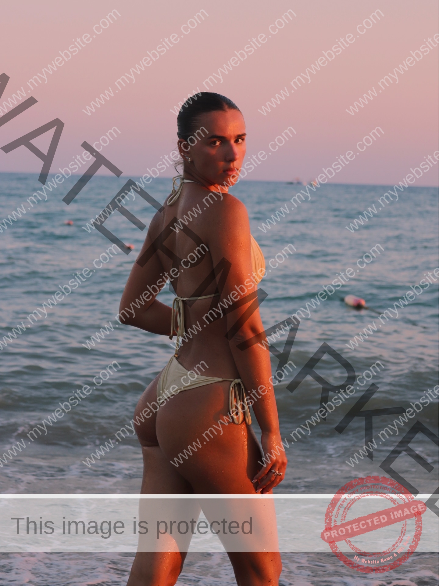 viktoriya-antipova-russia-viichkaaaaa-03768 Viktoriya Antapova, track and field star from Russia, in a beige bikini on the shore at sunset, ocean and waves glowing behind her.