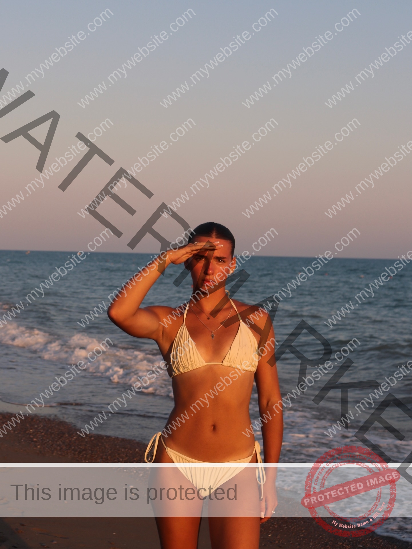 viktoriya-antipova-russia-viichkaaaaa-03774 Viktoriya Antapova, track and field star from Russia, stands on a sandy beach at sunset in a white bikini, saluting the camera.
