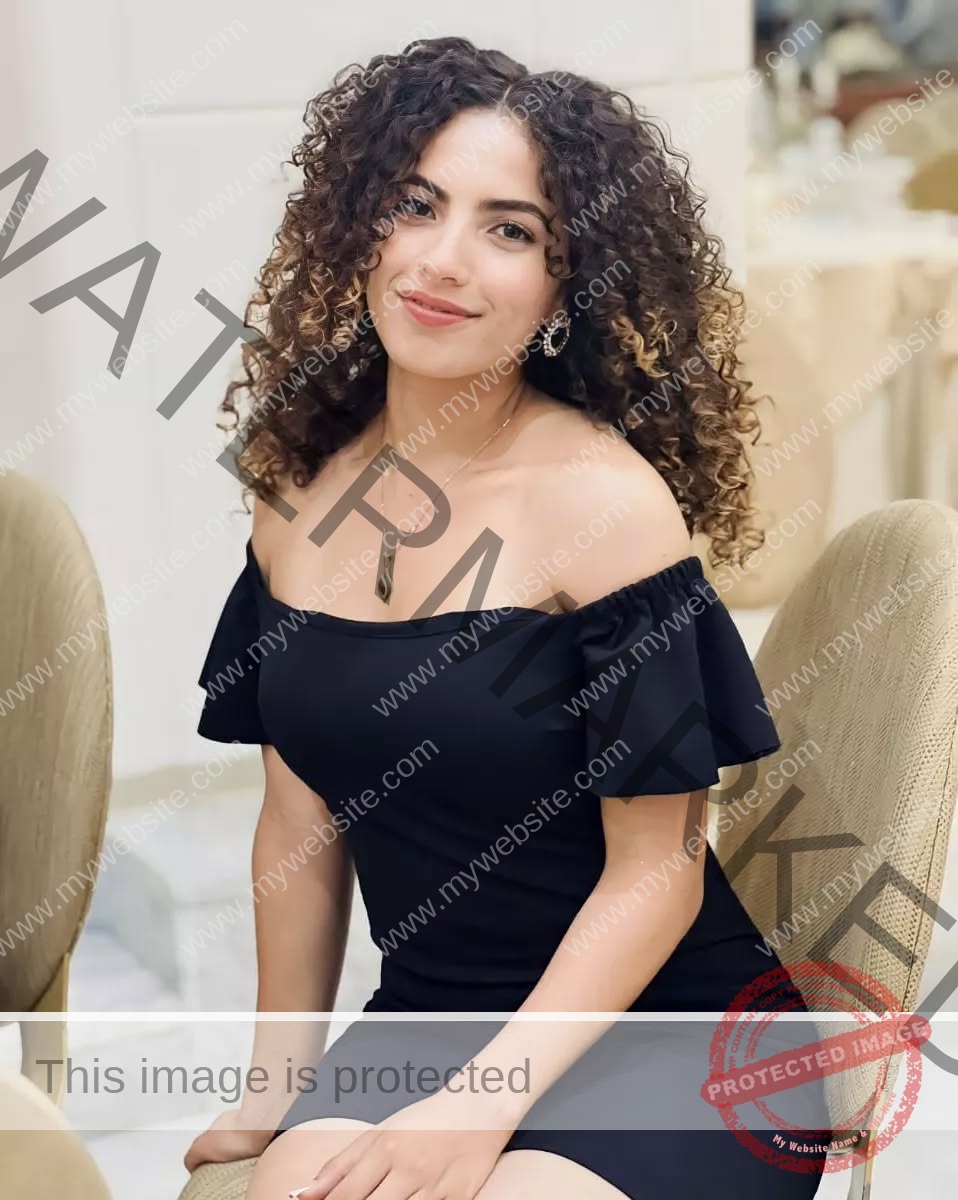 yassmine-baccar-tunisia-yassmine_baccar-08442 Yassmire Baccar, track and field star from Tunisia, with curly brown hair in a black off-shoulder dress, smiles on a tan chair.