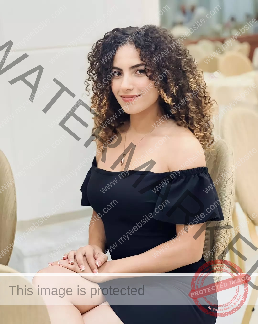 yassmine-baccar-tunisia-yassmine_baccar-08443 Yassmire Baccar, track and field star from Tunisia, with curly hair in a black dress smiles while seated on a light chair indoors.