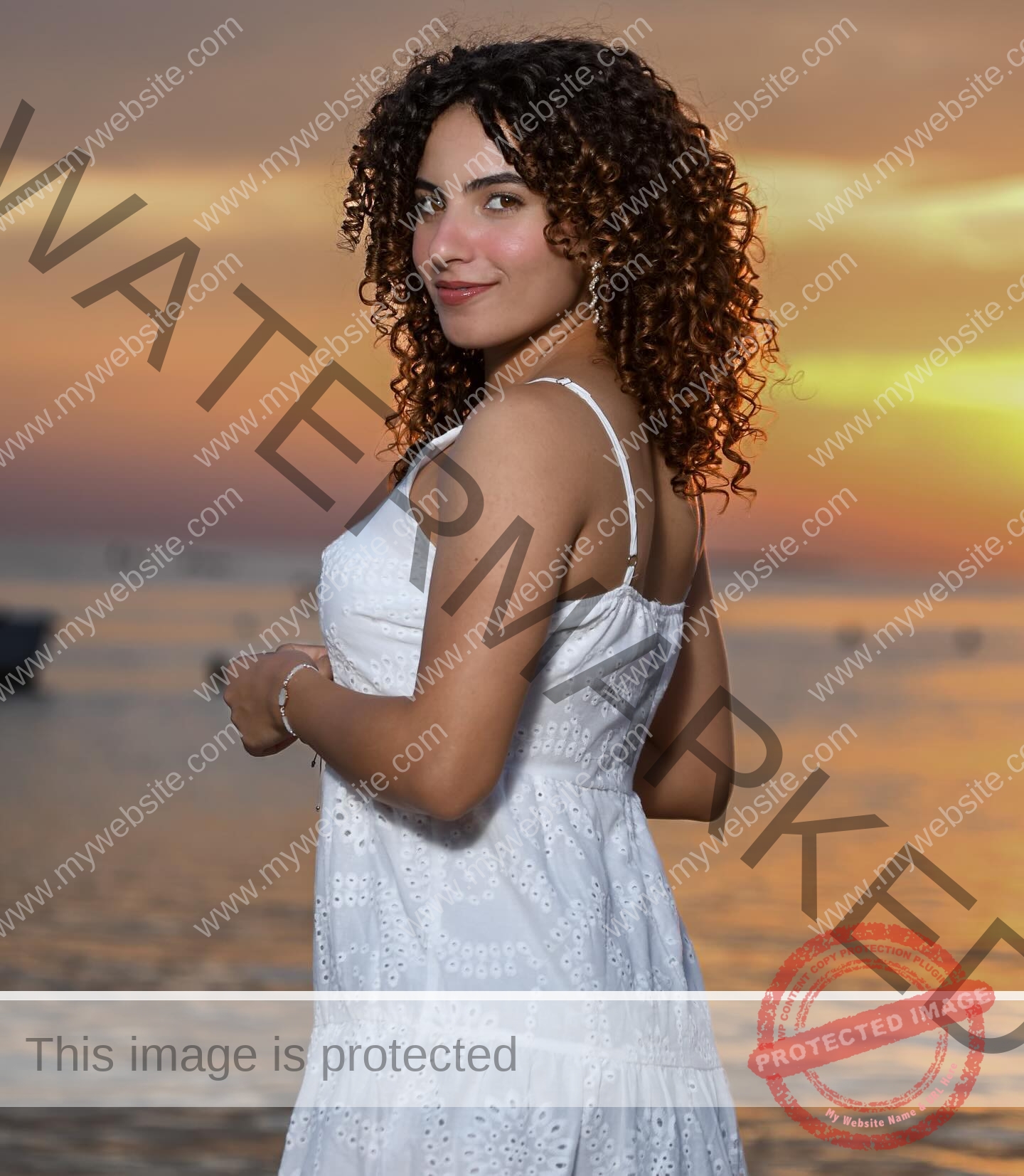 yassmine-baccar-tunisia-yassmine_baccar-08459 Yassmire Baccar, track and field star from Tunisia, with curly hair in a white dress stands by colorful sunset water, smiling back.