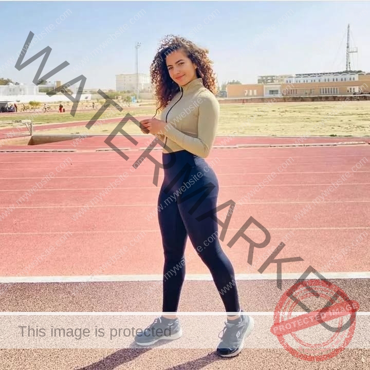 yassmine_baccartagged-08504 Yassmire Baccar, track and field star from Tunisia, with curly hair in beige top and black leggings poses on a red running track.