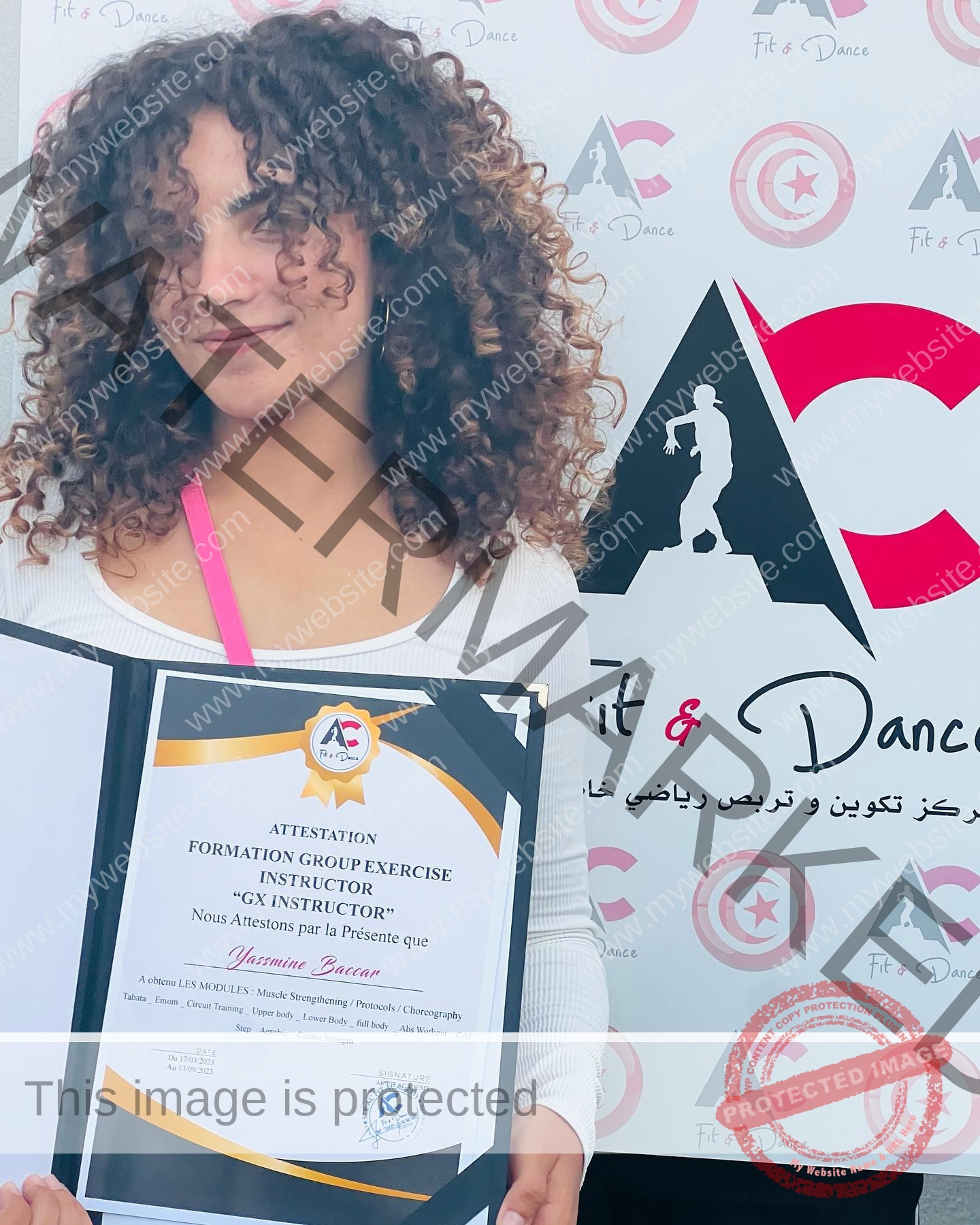 yassmine_baccartagged-08511 Yassmire Baccar, track and field star from Tunisia, holds a certificate and smiles before an AC Fit & Dance logo banner.