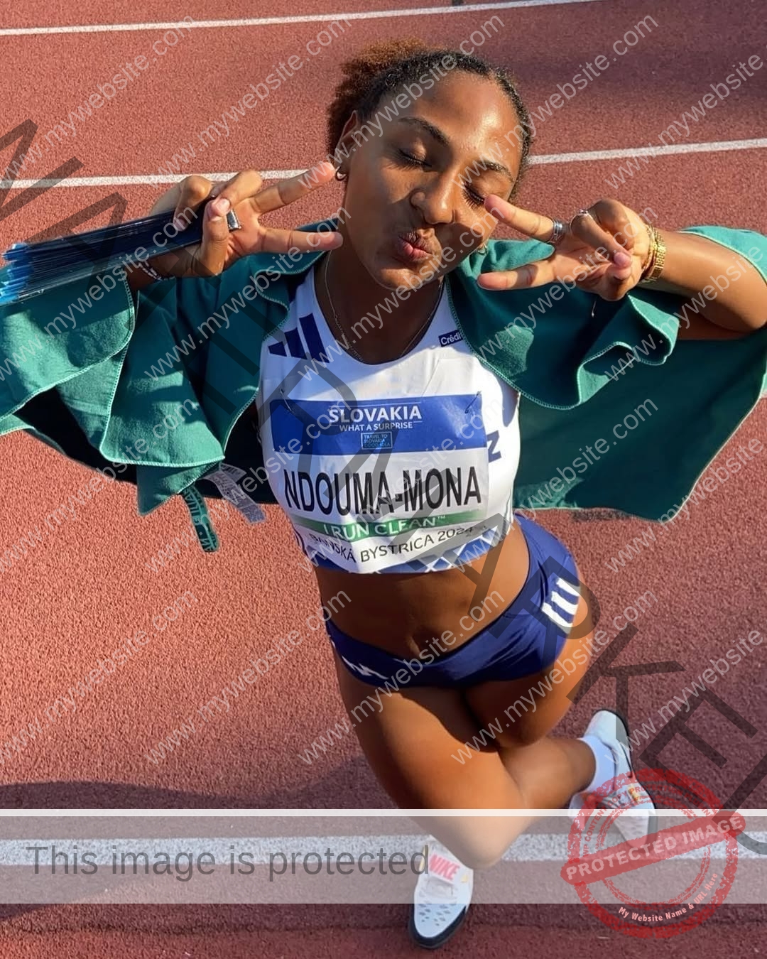 zola-ndouma-mona-france-zolaathle-09237 Zola Ndouma Mona, track and field star from France, stands on the track flashing peace signs and smiling eyes closed in her bib.