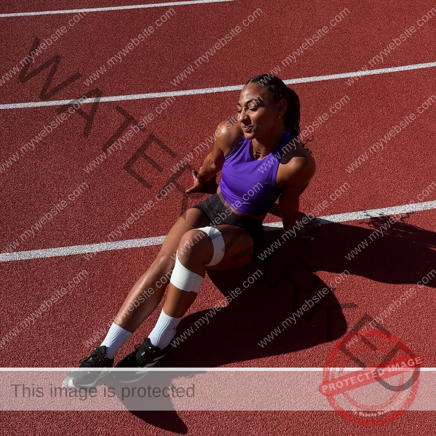 zola-ndouma-mona-france-zolaathle-09340 Zola Ndouma Mona, track and field star from France, sits on a sunny track in athletic gear with a bandaged knee and closed eyes.
