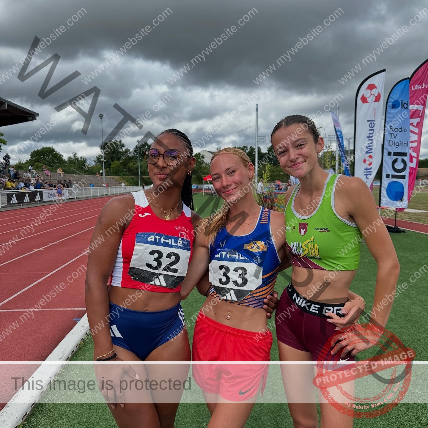 zola-ndouma-mona-france-zolaathle-09351 Zola Ndouma Mona, track and field star from France stands on a track with two teammates, all smiling in race bibs 32 and 33.