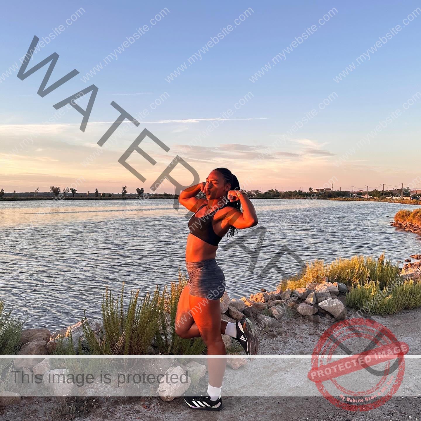 zola-ndouma-mona-france-zolaathle-09380 Zola Ndouma Mona, track and field star from France, stretches by the water at sunset on a gravel path, sky clear with soft clouds.