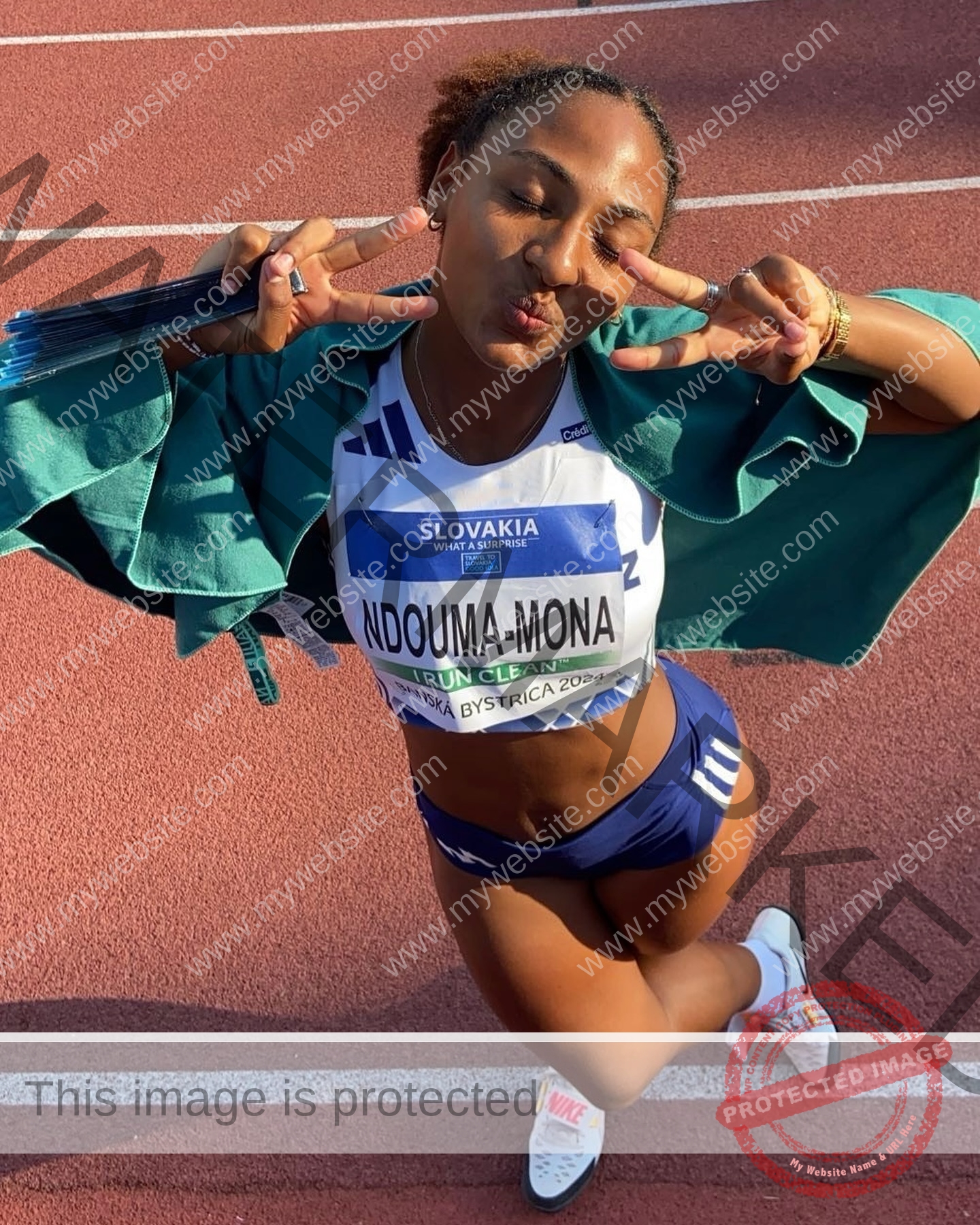 zola-ndouma-mona-france-zolaathle-09448 Zola Ndouma Mona, track and field star from France, playfully poses on a track, flashing peace signs with eyes closed in running gear.