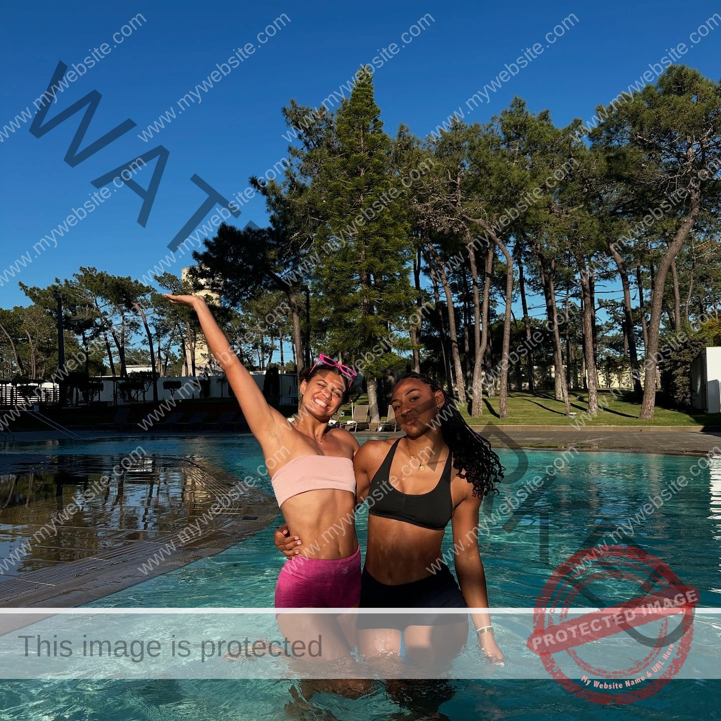 zola-ndouma-mona-france-zolaathle-09464 Zola Ndouma Mona, track and field star from France, smiles in a pool with a friend, both in swimsuits under tall trees and blue sky.