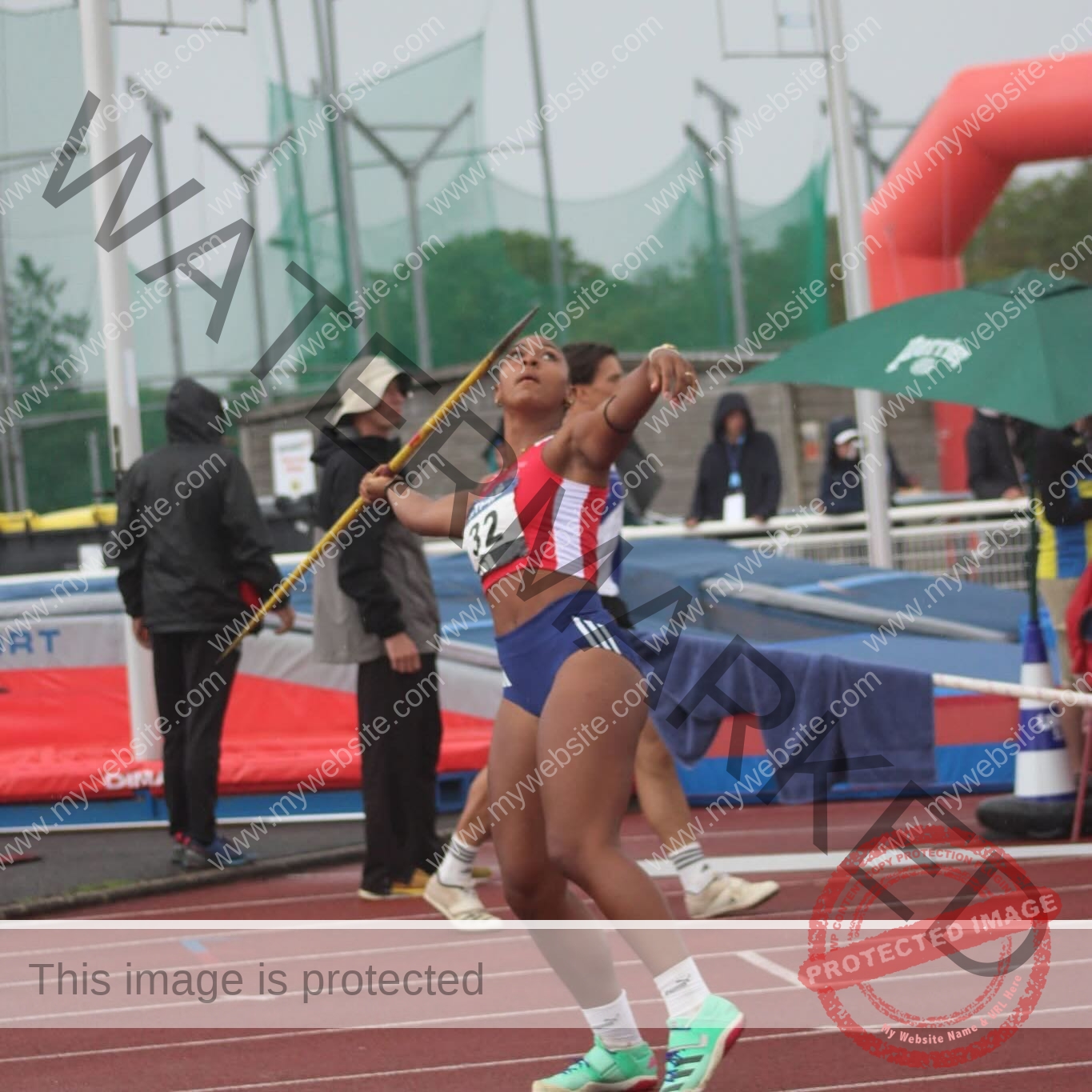 zola-ndouma-mona-france-zolaathle-09470 Zola Ndouma Mona, track and field star from France, prepares to throw a javelin on a track in red, white, blue uniform.