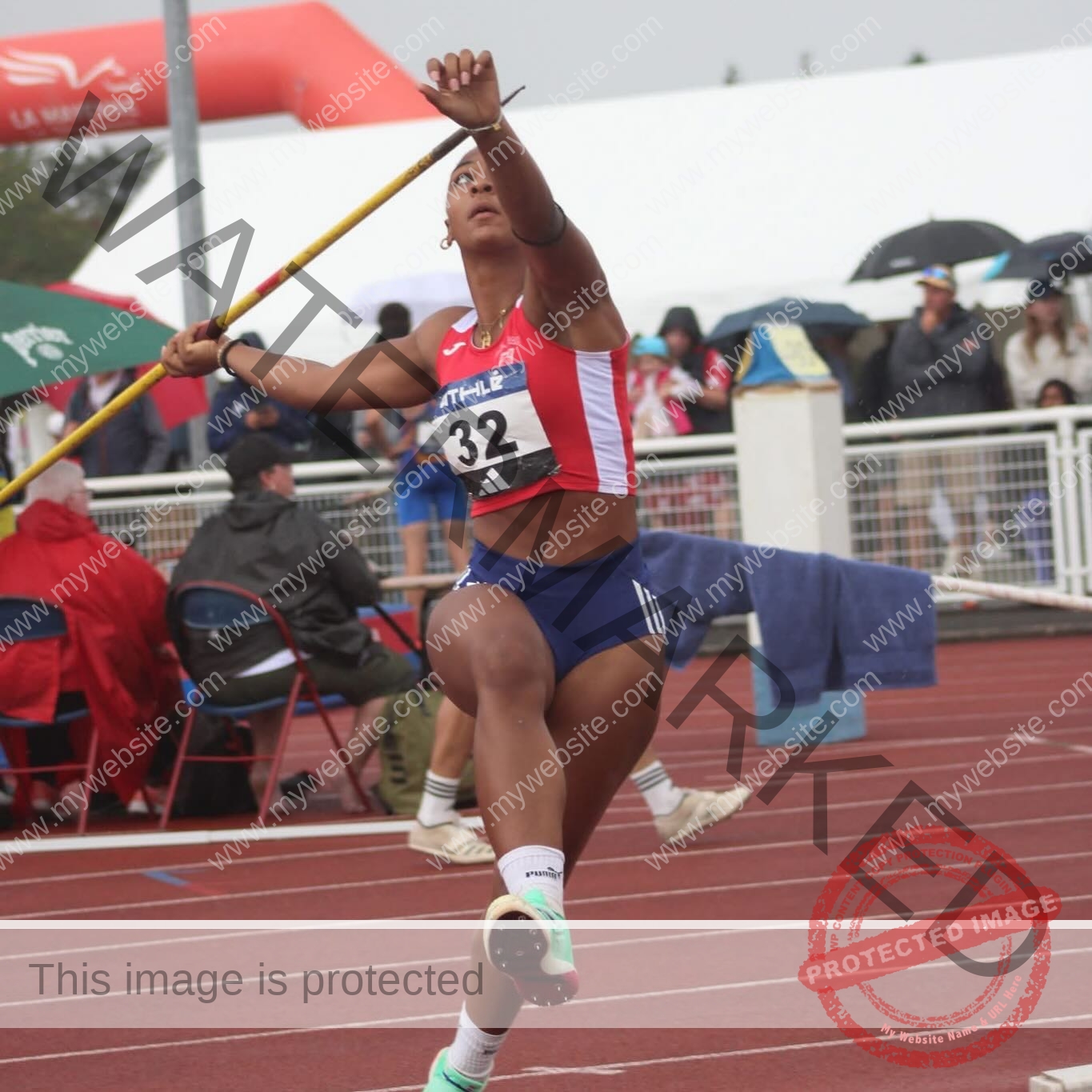 zola-ndouma-mona-france-zolaathle-09473 Zola Ndouma Mona, track and field star from France, throws a javelin on the track in red, white, blue uniform; crowd behind.