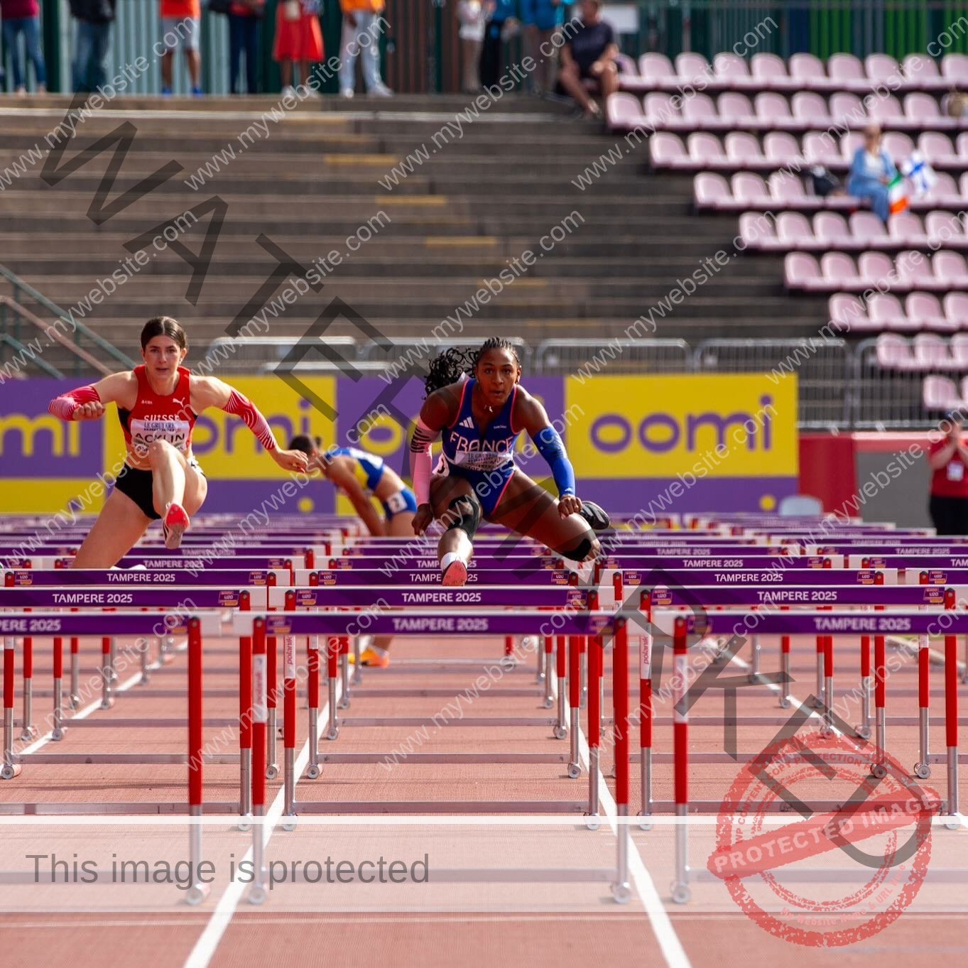zola-ndouma-mona-france-zolaathle-09482 Zola Ndouma Mona, track and field star from France, leaps mid-air over hurdles in a race beside another competitor on an outdoor track.