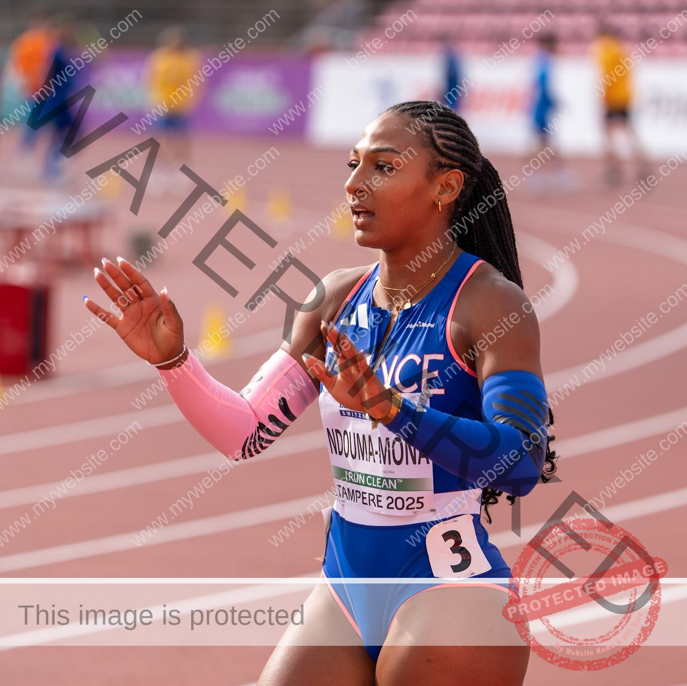 zola-ndouma-mona-france-zolaathle-09485 Zola Ndouma Mona, track and field star from France raises her hands on the track in bib number 3, braids, blue and pink uniform.
